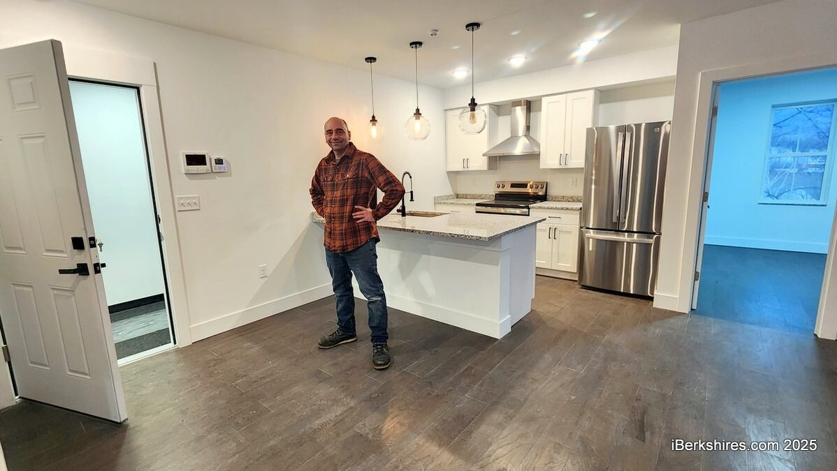 A finished apartment at 20 East Street — white shaker kitchen with granite counters, an island, pendant lights and stainless appliances